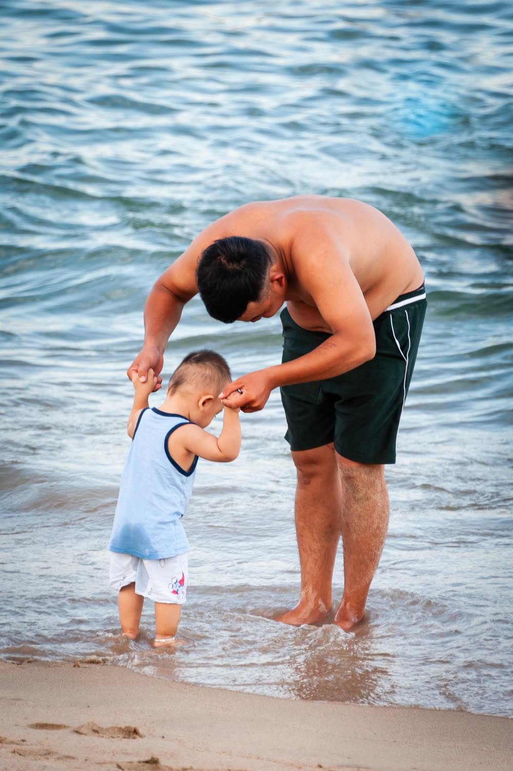 Pai a segurar as mãos do filho à beira-mar